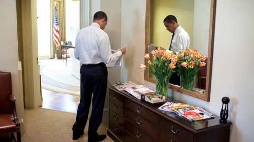 President Barack Obama standing and reading a paper in the White House